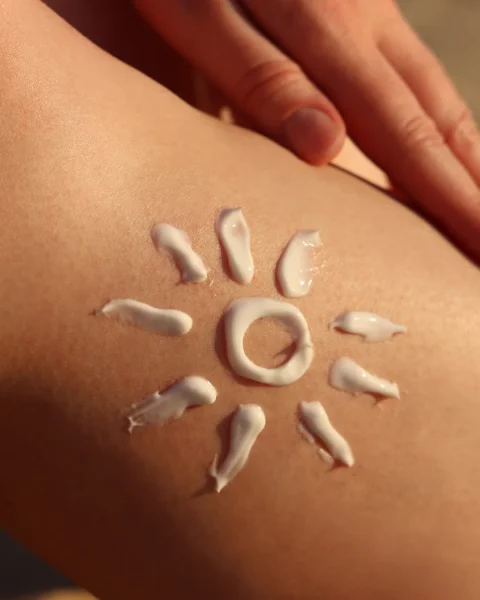 Cream sunscreen dolloped in a sun shape on skin: a central circular ring with radiating droplets forming sun rays