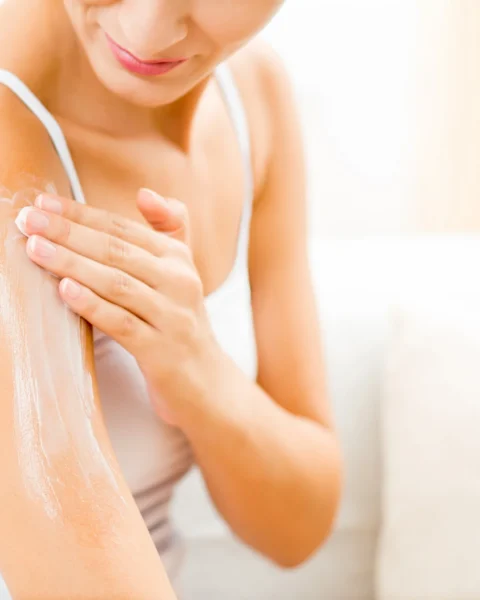 Woman applying lotion to her forearm, smoothed with a moisturizer in a bright, airy setting